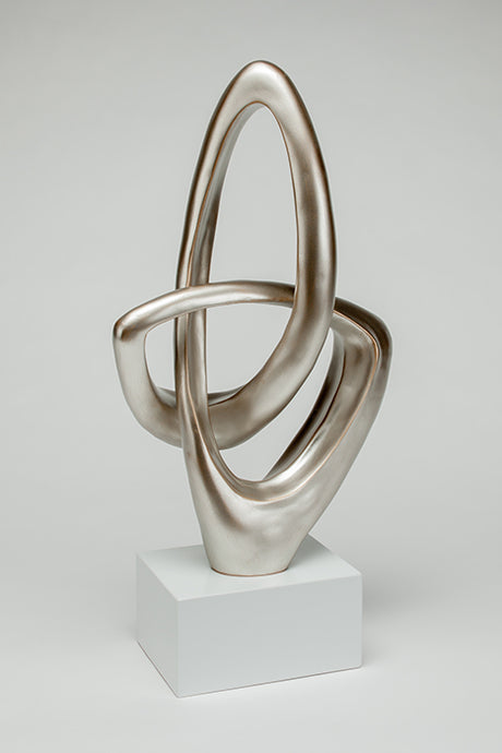 Abstract silver sculpture on a white pedestal against a light gray background