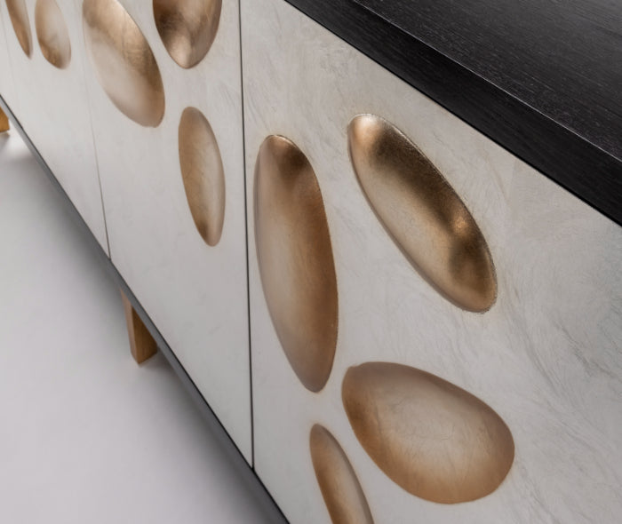 Close-up of a furniture piece with gold oval decorations on a light wood background.