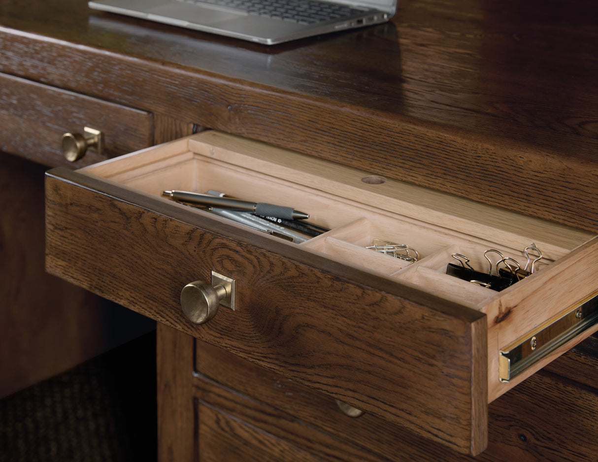 Wooden desk with open drawer containing office supplies, laptop in the background