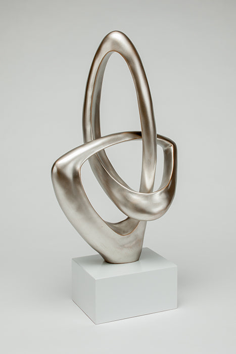 Abstract silver sculpture on a white pedestal against a light gray background