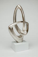 Abstract silver sculpture on a white pedestal against a light gray background