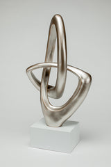 Silver abstract sculpture on a white pedestal against a light gray background
