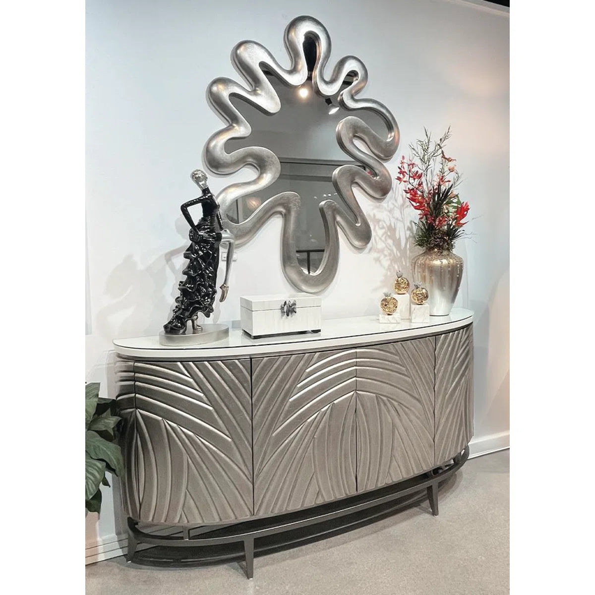 Decorative console table with leaf-patterned design, featuring a large mirror and decorative items.