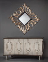 Decorative wall mirror with a sunburst design above a wooden cabinet against a gray background